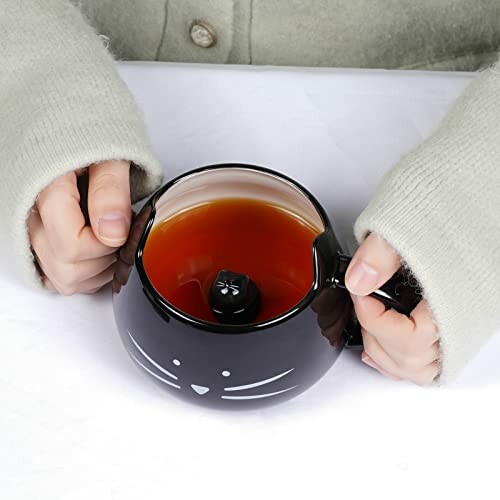 Person holding a black cat-shaped mug filled with tea.