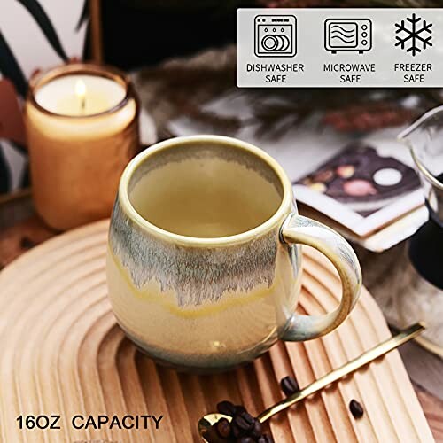 Ceramic mug with coffee next to a candle on a wooden surface, featuring dishwasher, microwave, and freezer safe icons.