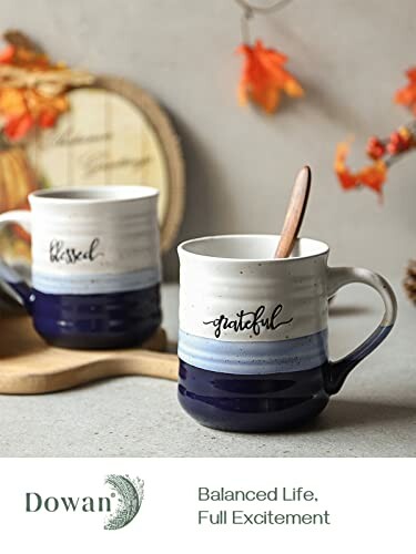 Two ceramic mugs with 'blessed' and 'grateful' text, wooden spoons inside, autumn decor