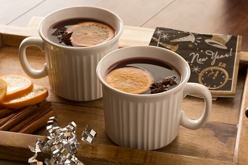 Two mugs of mulled wine with orange slices and spices on a wooden tray.