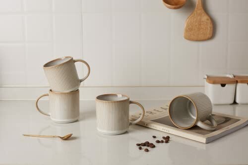 Stacked ceramic mugs on a kitchen counter with coffee beans and spoon.